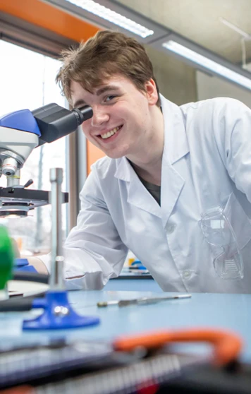 Student using a microscope in a science classroom filled with lab equipment and colourful bottles. Student using a microscope in a science classroom filled with lab equipment and colourful bottles.